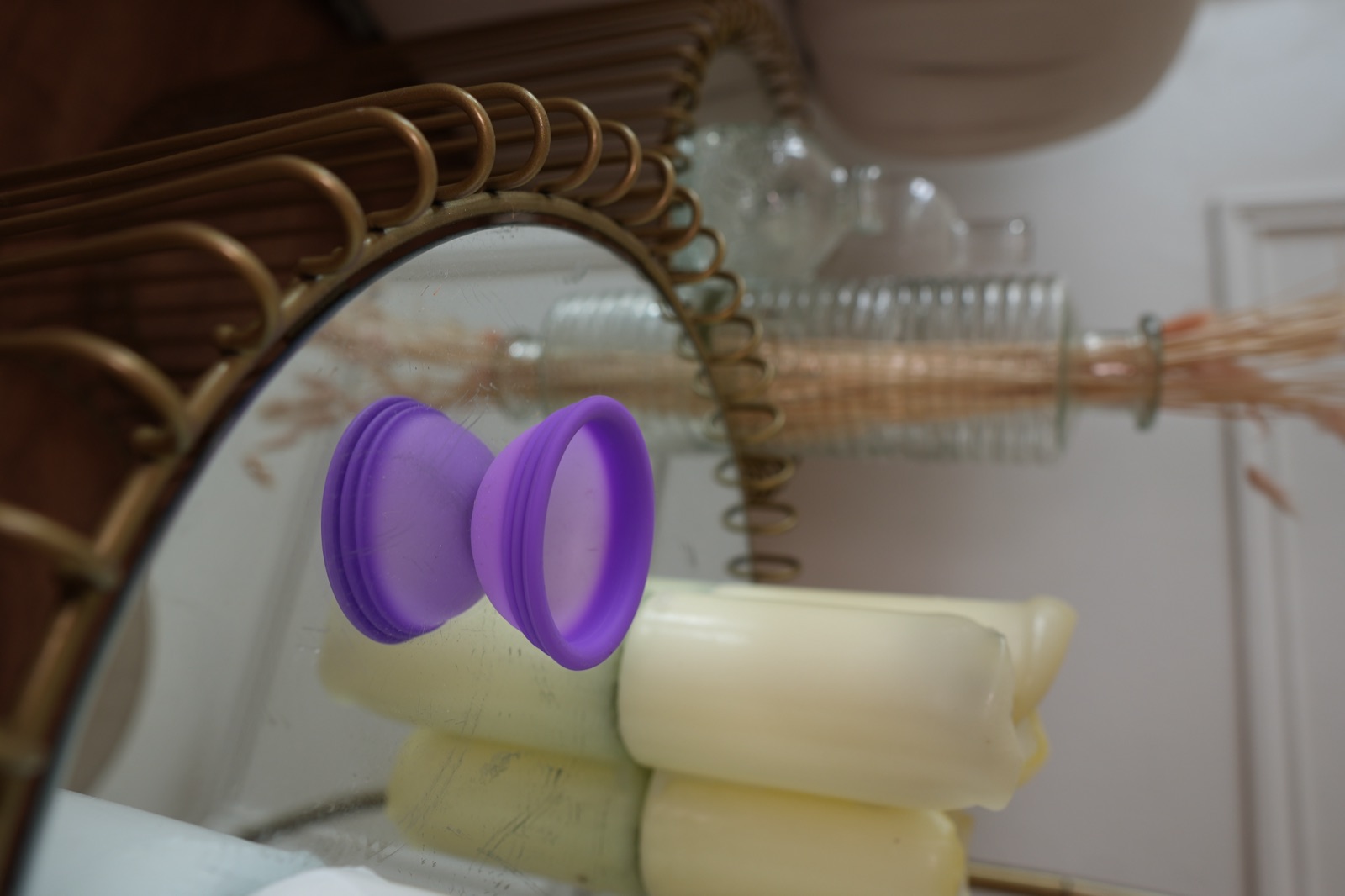 A purple menstrual disc on a mirrored side table beside candles